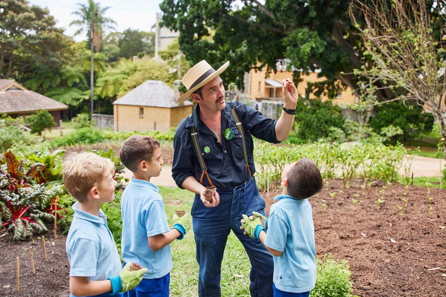 CPD Damien Egan showing a bean seed to students wearing gardening gloves in the kitchen garden.