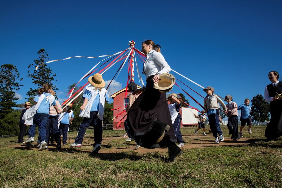 Children and adults dressed in period costume holding ribbons attached to pole.