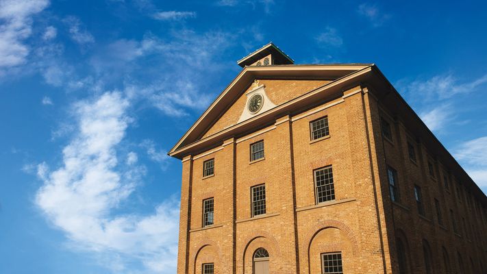 Front of colonial era two storey brick building with blue sky behind.