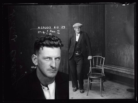 Dual mugshot in black and white; man seated and then man standing, with cap on.