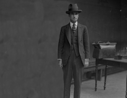 A man stands looking at the camera with a large black bag next to him.